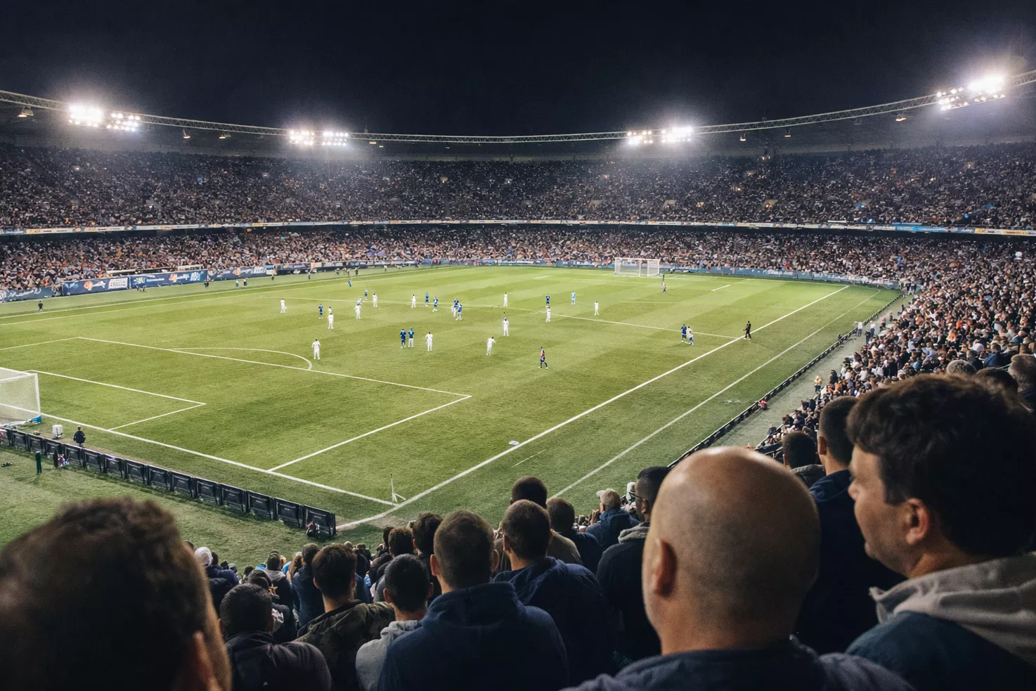 Tifosi nello stadio che guardano una partita di calcio in corso sotto le luci dei riflettori
